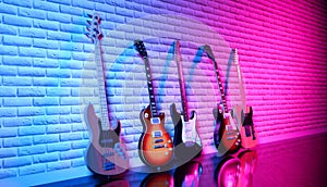 Several electric guitars against a brick wall in neon light