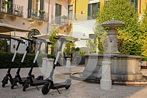 Several electric scooters for rent by tourists and citizens stand in rows on the sidewalk of the old city