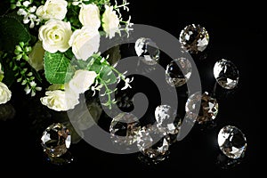 Several excellent pure diamonds and bouquet of white roses with reflection on black mirror background close up view. Jewelry