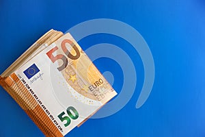 Several folded 50 Euro banknotes on a bright blue background. Free space for text.