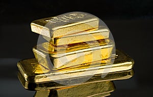 Several gold bars of different weight on a dark mirror surface