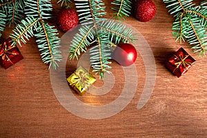 Several green spruce branches with red Christmas balls, Christmas-tree decorations and small gifts on a wooden background. Flat