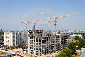Several high-rise cranes at a construction site, together with people, are building a modern apartment building.
