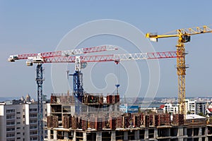 Several high-rise cranes at a construction site, together with people, are building a modern apartment building.