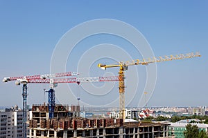 Several high-rise cranes at a construction site, together with people, are building a modern apartment building.