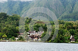 Several houses build at the foot of a mountain next to a lake in Sumatra Samosir Island.