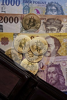Several Hungarian forint paper money denominations, with gold bitcoin digital cryptocurrency coin on a blue background
