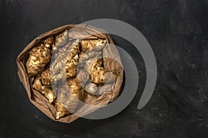 Several Jerusalem artichoke tubers in a paper bag on a black background with copy space. Helianthus tuberosus. Top view