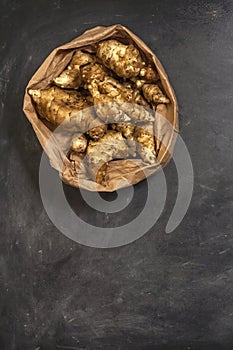 Several Jerusalem artichoke tubers in a paper bag on a black background with copy space. Helianthus tuberosus. Top view