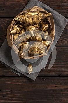 Several Jerusalem artichoke tubers in a paper bag on a wooden table with copy space. Helianthus tuberosus. Top view. Vertical