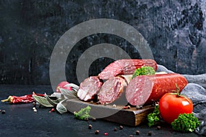 Several kinds of sausage, fresh vegetables and greens on a black background.