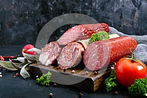 Several kinds of sausage, fresh vegetables and greens on a black background.