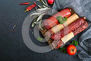 Several kinds of sausage, fresh vegetables and greens on a black background.