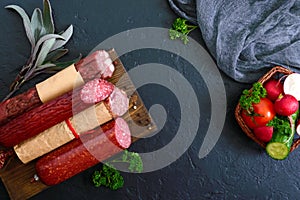 Several kinds of sausage, fresh vegetables and greens on a black background.