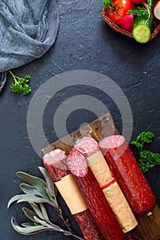 Several kinds of sausage, fresh vegetables and greens on a black background.