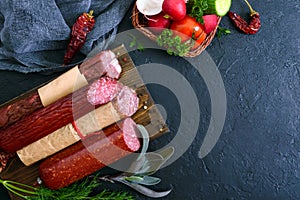 Several kinds of sausage, fresh vegetables and greens on a black background.