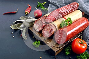 Several kinds of sausage, fresh vegetables and greens on a black background.