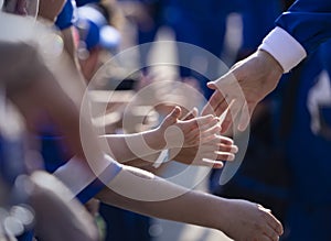 Several Little children giving high fives to their sports heroes outside of a sports arena as they walk by.