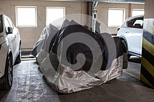 Several motorcycles stand in row covered with dust protective canvas covers for safekeeping during winter