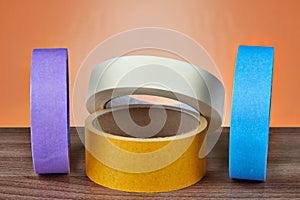 Several multi-colored rolls of adhesive tape on an orange background.
