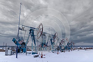 Several Oil pumpjack under gray heavy leaden clouds winter working. Oil rig energy industrial machine for petroleum in the sunset