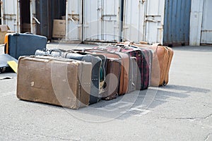 Several old suitcases clothes are on asphalt.