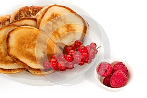 Several pancakes with red currants and raspberries on plate on white background. Full depth of field