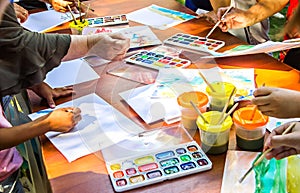 Several of people draw on paper using watercolor paints sitting at the same table. Drawing Masterclass.