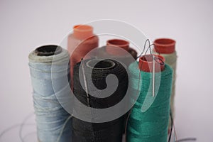 Several piles of sewing thread spools of various colors isolated on a white background and also with small sewing needles