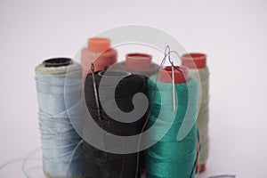 Several piles of sewing thread spools of various colors isolated on a white background and also with small sewing needles