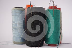 Several piles of sewing thread spools of various colors isolated on a white background and also with small sewing needles