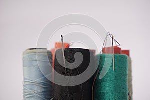 Several piles of sewing thread spools of various colors isolated on a white background and also with small sewing needles