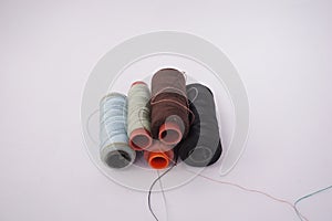 Several piles of sewing thread spools of various colors isolated on a white background and also with small sewing needles