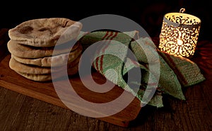 Several pita breads or arabian bread stacked on a rustic cloth and a cutting board on a wooden table with black background with