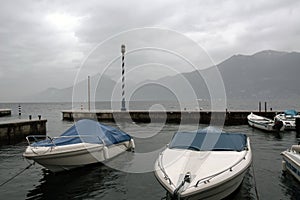 Several pleasure boats at the pier in the cold sea. In the background are mountains in the fog