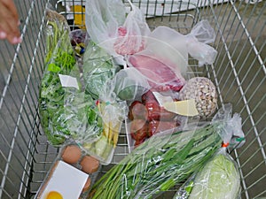 Several raw food ingredients, in a shopping cart, being bought at a supermarket