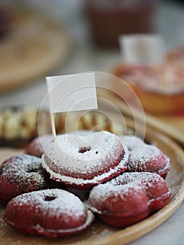 Several red velvet heart-shaped donuts on top icing placed in a wooden plate stick white paper flag, snacks sweet food delicious