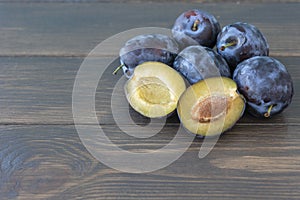 several ripe plums lie on dark wooden background, one plum is cutted on halfs.