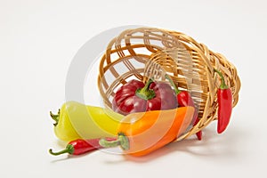 Several ripe sweet and hot peppers in a straw basket on a white