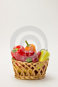 Several ripe sweet and hot peppers in a straw basket on a white
