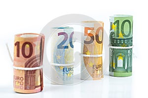 Several rolls of euro banknotes stacked by value from ten, twenty, fifty and one hundred euros isolated on white background.