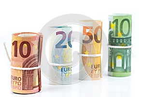 Several rolls of euro banknotes stacked by value from ten, twenty, fifty and one hundred euros isolated on white background.