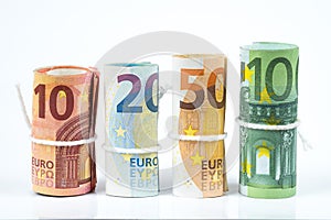 Several rolls of euro banknotes stacked by value from ten, twenty, fifty and one hundred euros isolated on white background.