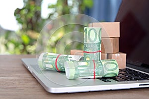 Several rolls of euro bills and a model of a courier box are placed on the opened laptop keyboard