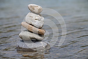 Several round pebbles of different sizes are stacked on top of each other. They form a pyramid. The stones stand in shallow water
