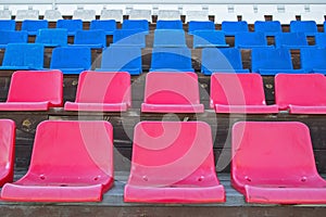 Several rows of plastic seats in red, blue and white colors mounted on brown-painted wooden platforms on podium of village stadium