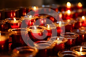 Several rows of burning votive candles in a dark European Catholic church in Rome Italy seeking favor from the Lord or