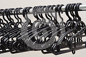 Several same similar all black plastic cloth hangers on a horizontal aluminium pole