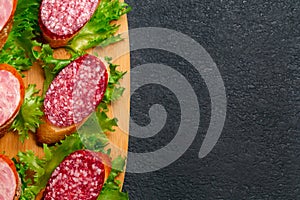 Several sandwiches with sausage and salami and sauce on a black board, flat lay background with copyspace