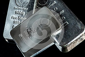 Several silver bars of different weight on a dark mirror surface.